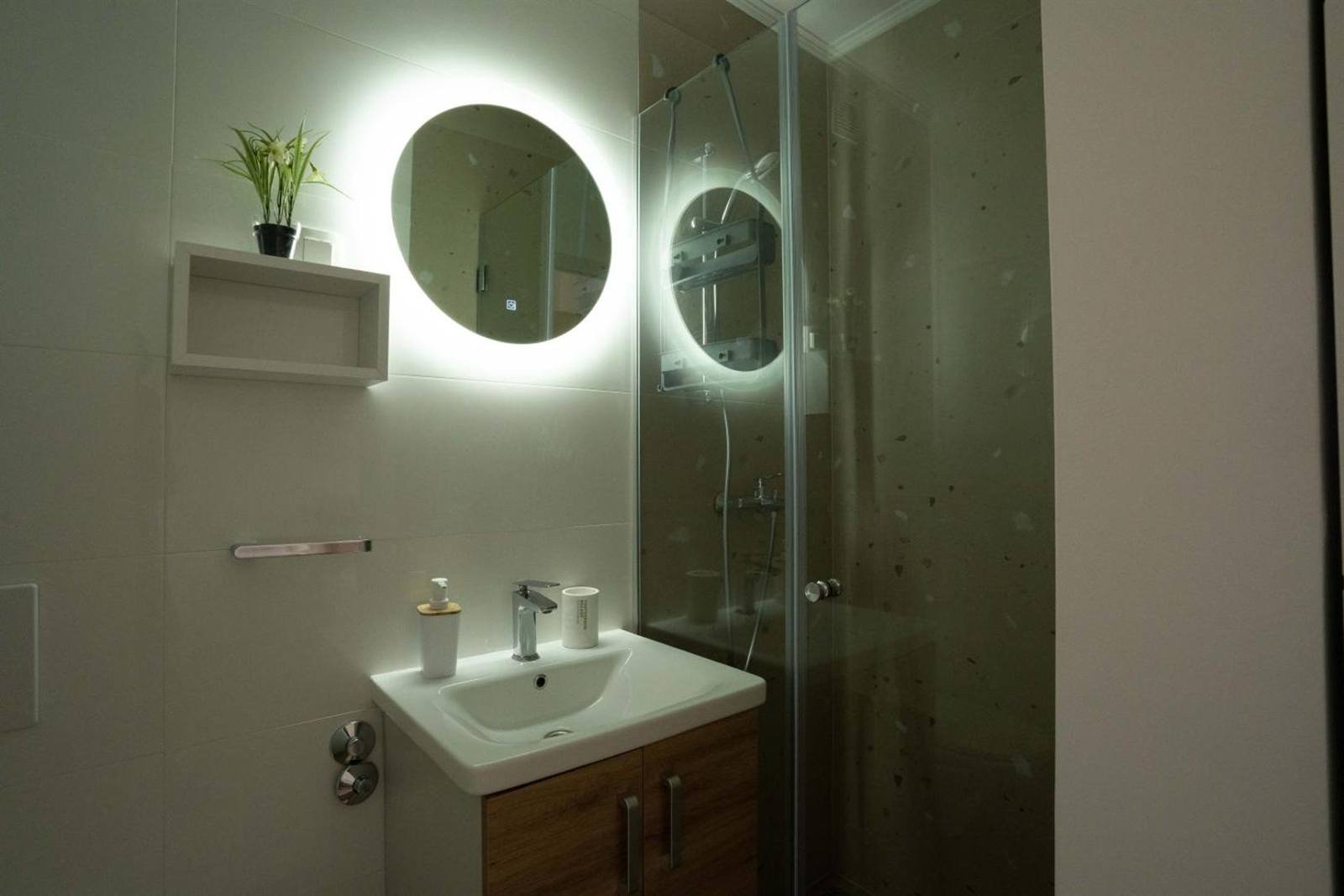 Apartments & Rooms Petra: bathroom with a glass shower and a lit round mirror